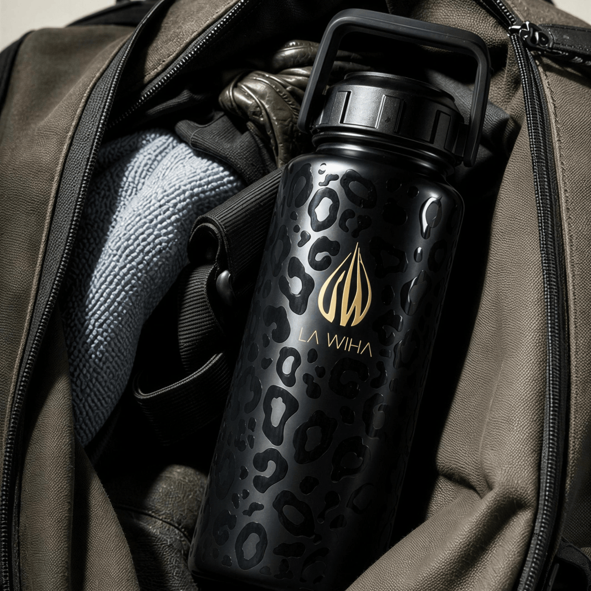 A 32 ounce black stainless steel La Wiha water bottle with a gold logo and leopard print pattern, shown inside an open olive green backpack, workbag, gym bag, suitcase, duffel bag, airport , travel, traveler