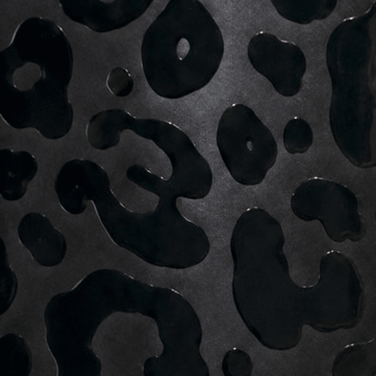 A close-up of a glossy 3D printed black leopard print pattern on a dark black background.
