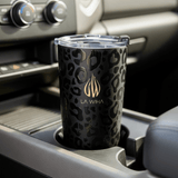 A black 20 ounce leopard print insulated tumbler with a clear lid sits in a car cup holder perfectly. The cup features a gold logo and the text 'LA WIHA'.