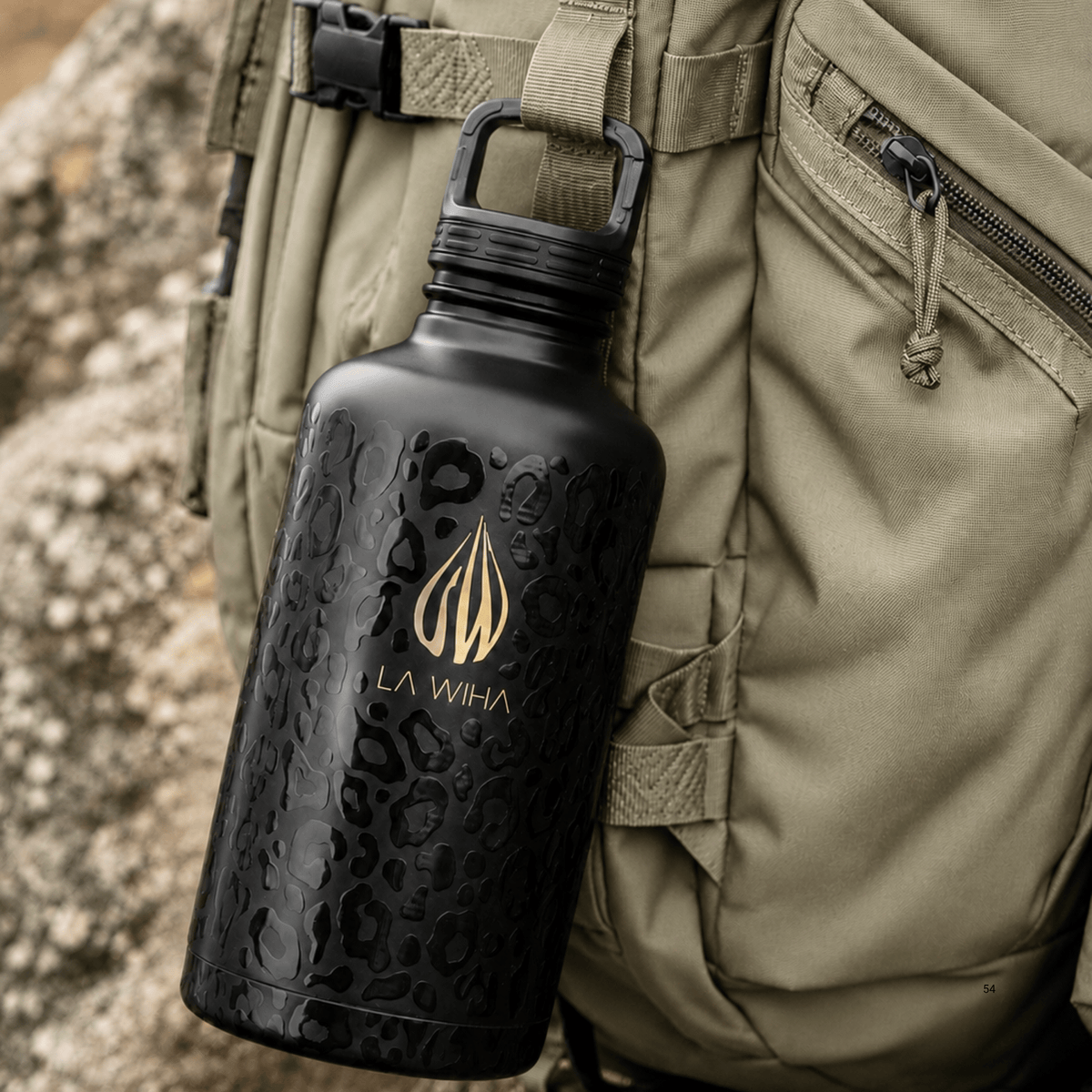 A black La Wiha insulated water bottle with a gold logo and subtle dark pattern, carabiner clip hanging from a khaki outdoor backpack strap against a rocky, mountains, hiking, backpacking background.